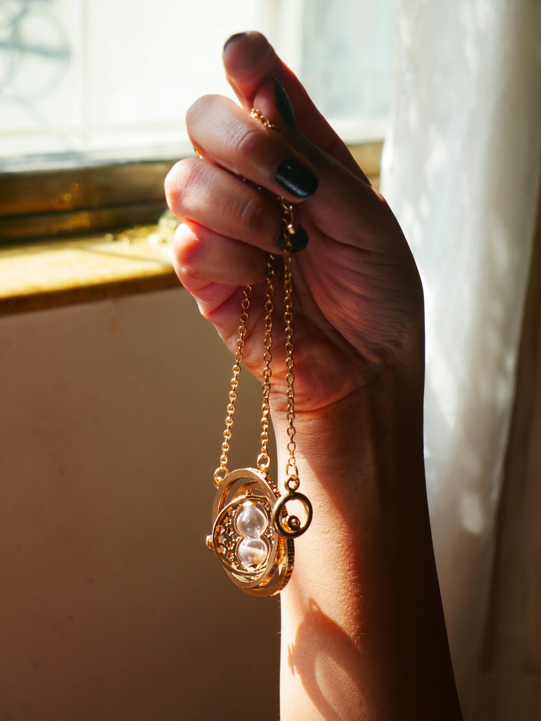 Mano con smalto scuro tiene una collana con ciondolo a clessidra dorata.