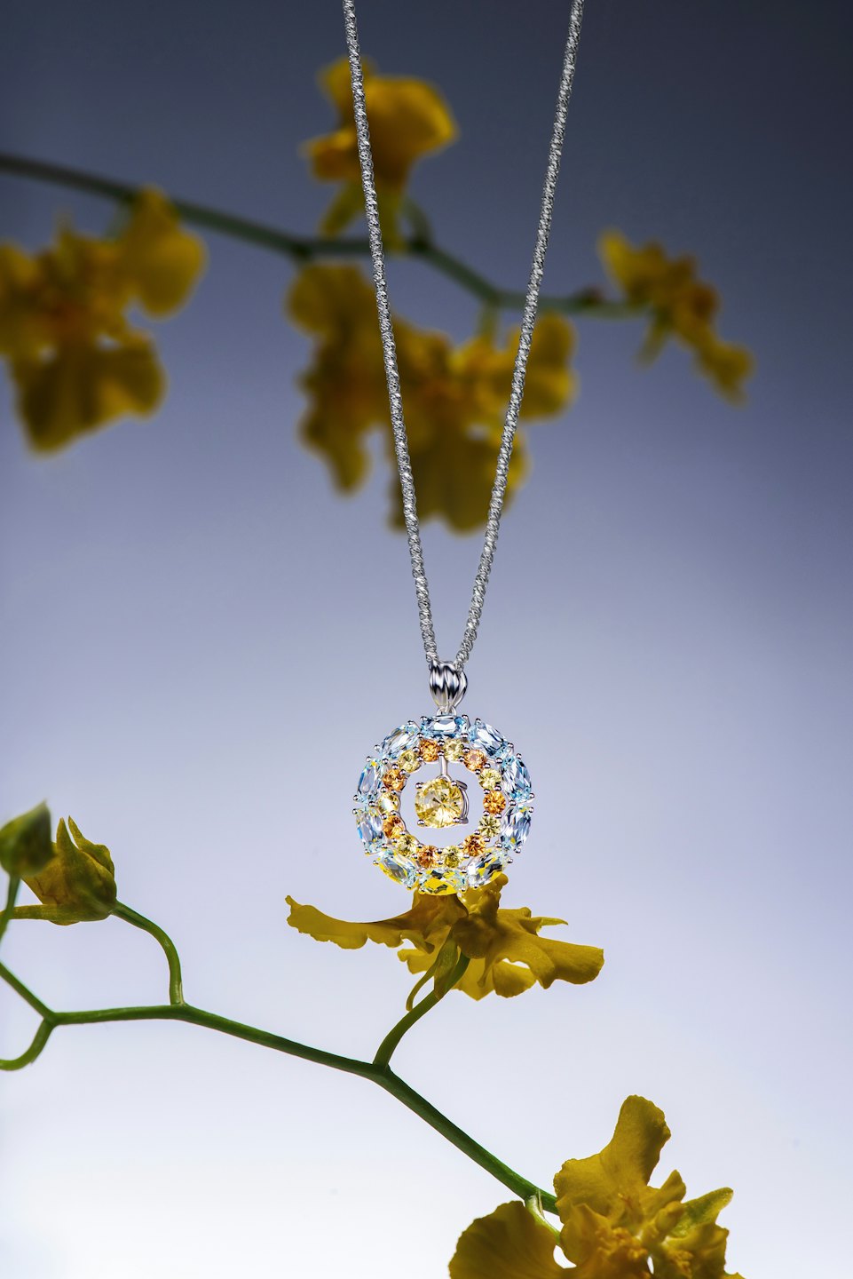 Collana d'argento con pendente di pietre preziose multicolori vicino a orchidee gialle.