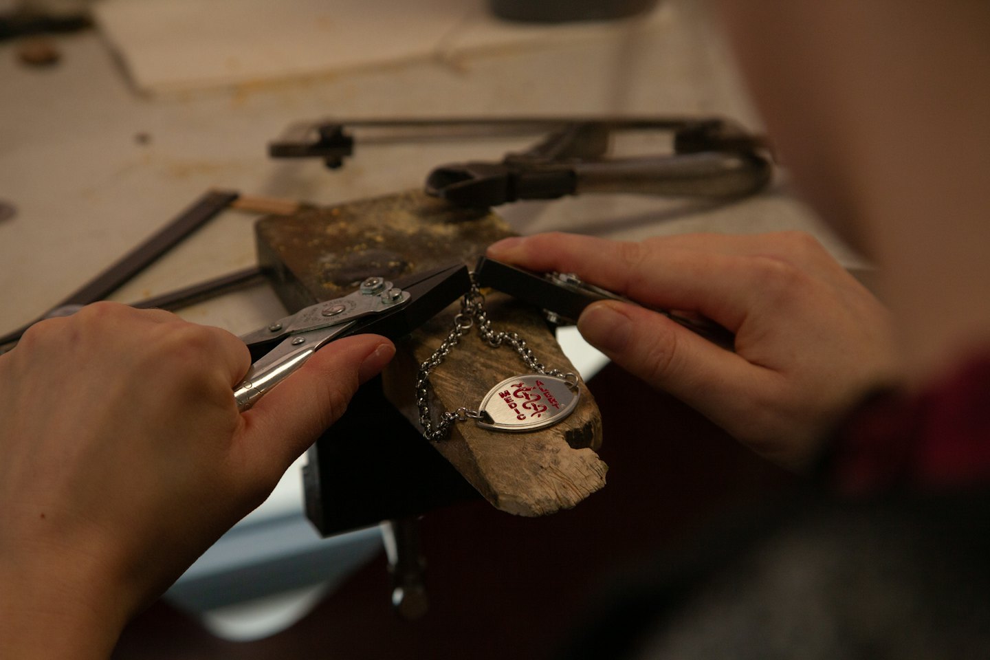 Mani che usano una pinza per creare una delicata collana di metallo su un banco da lavoro.